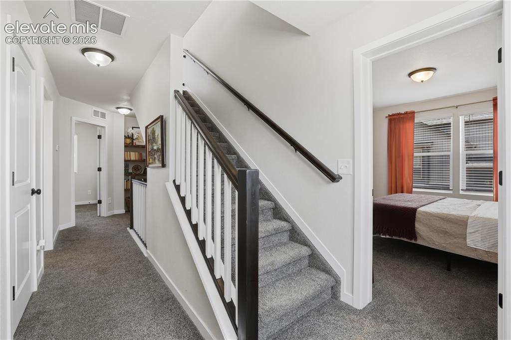 Image 33 of 48: Interior staircase with carpeted treads and dark wood banister, featuring w