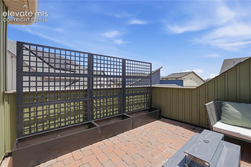 Image 40 of 48: Rooftop patio featuring brick paver flooring, a dark metal trellis system w