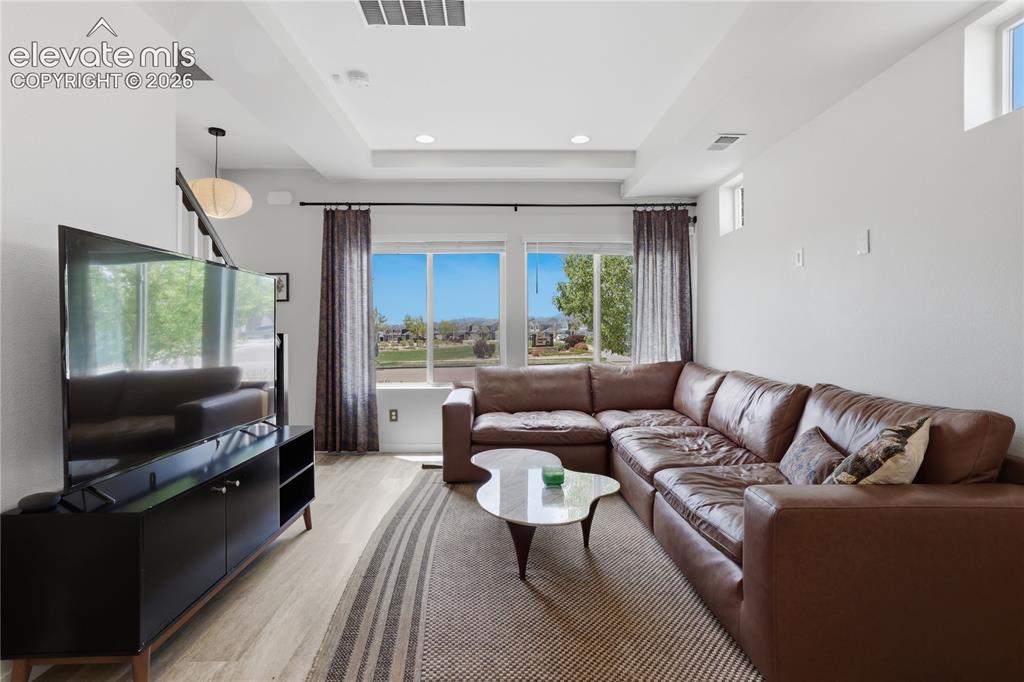 Image 9 of 48: Living area with wood-finish flooring, recessed lighting, and a tray ceilin