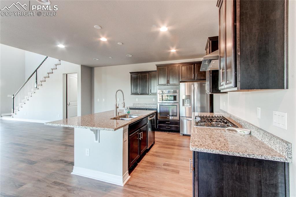 Image 22 of 49: Kitchen with light stone counters, stainless steel appliances, light wood f
