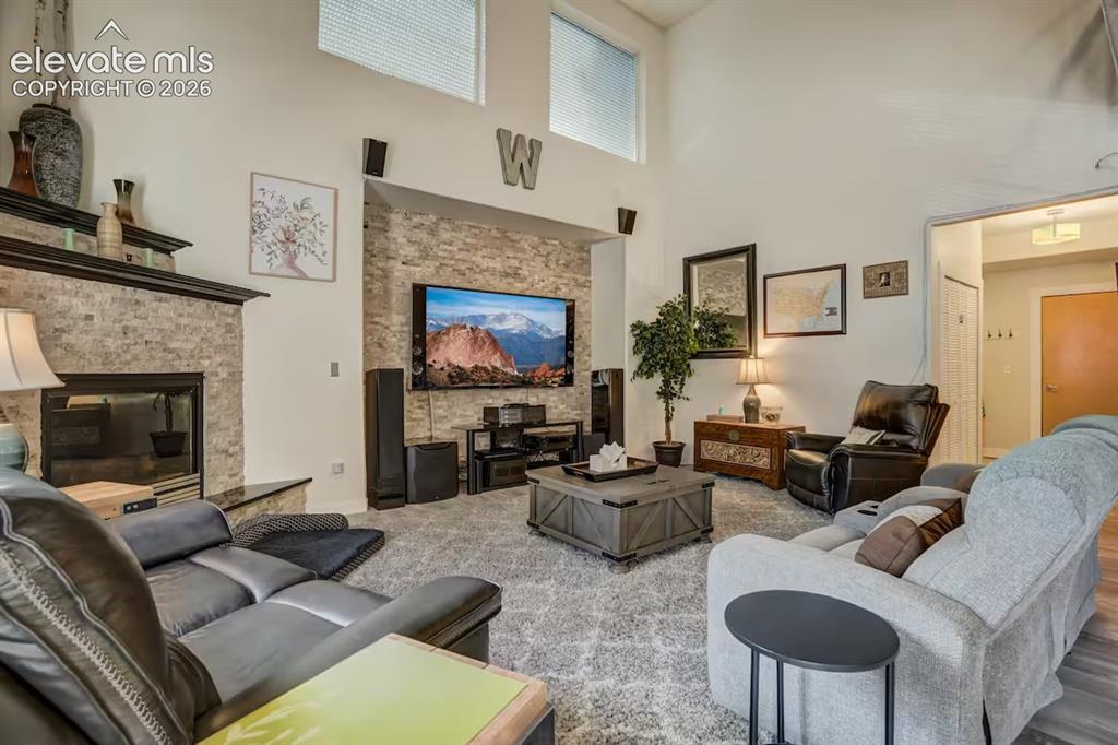 Image 11 of 45: Living room featuring a stacked stone fireplace with a dark mantel, a compl
