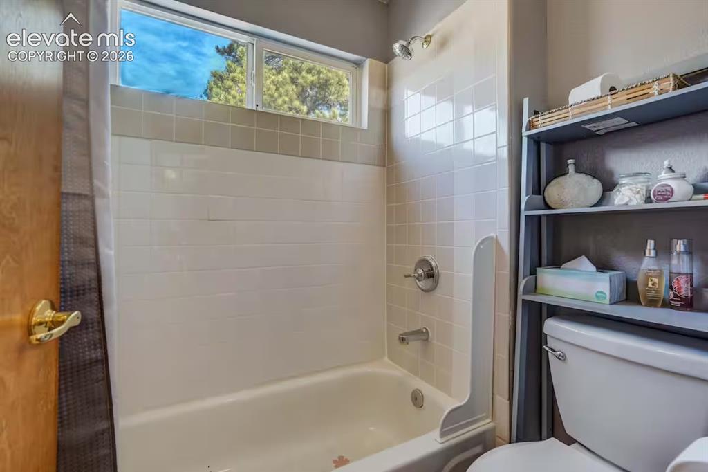 Image 29 of 45: Full bathtub with white tile surround and integrated shower head