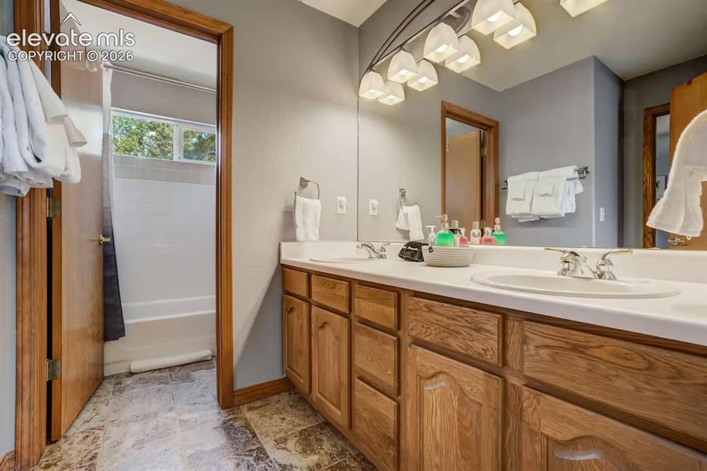 Image 33 of 45: Bathroom featuring a dual-sink vanity with wood cabinetry, a large mirror,