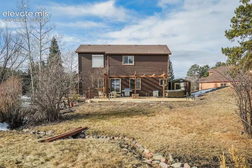 Image 39 of 45: Rear exterior featuring brown siding, a ground-level patio with a wooden pe