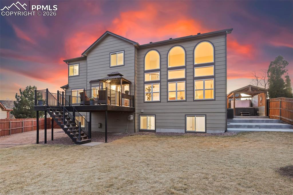 Image 2 of 50: Back of property at dusk with a fenced backyard, a patio, and a deck
