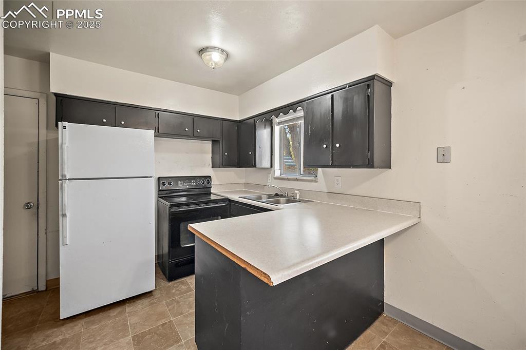 Image 12 of 19: Kitchen with freestanding refrigerator, light countertops, black range with