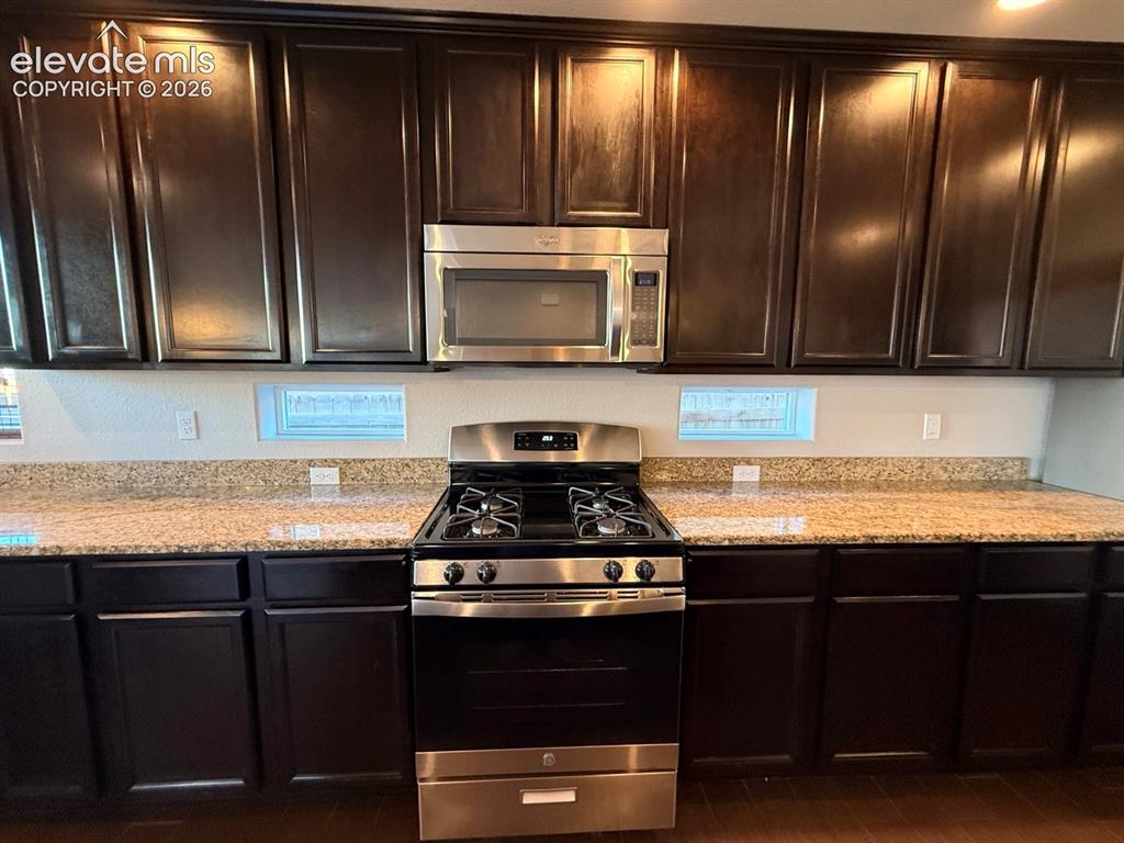 Image 10 of 50: Dark wood-finish cabinetry, light-toned countertops, stainless steel gas ra