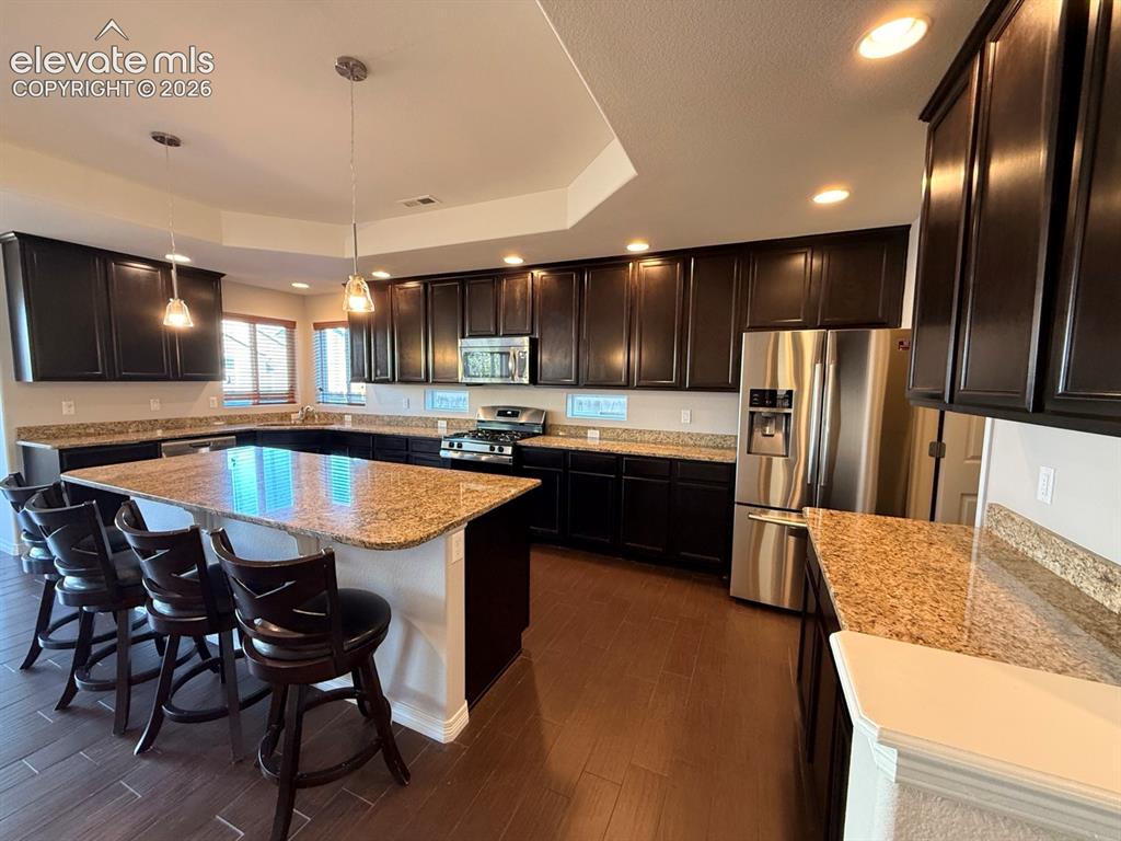 Image 8 of 50: Expansive kitchen featuring a large central island with seating, dark wood 