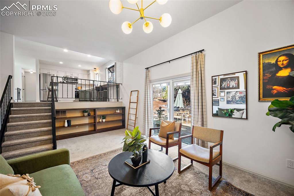 Image 15 of 45: Living area with a white brick fireplace, light carpet, and a chandelier