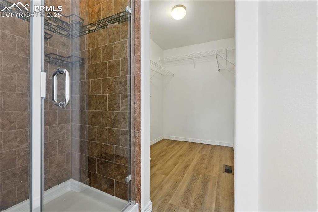 Image 18 of 46: Bathroom featuring a stall shower, wood finished floors, a spacious closet,