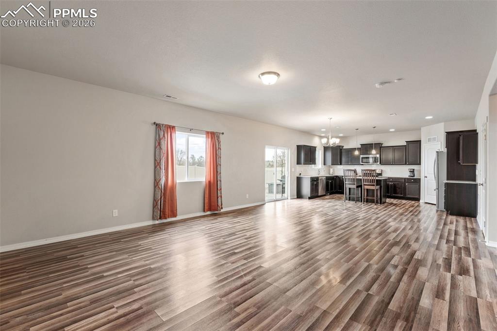 Image 16 of 50: Unfurnished living room with a chandelier and dark wood-style flooring