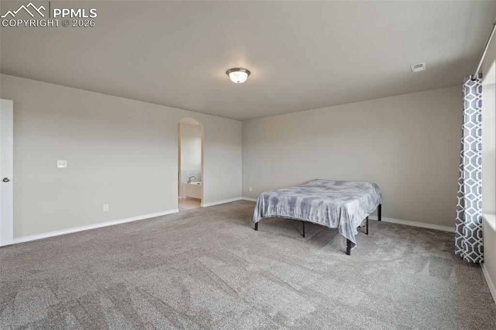 Image 34 of 50: Carpeted bedroom featuring arched walkways and connected bathroom