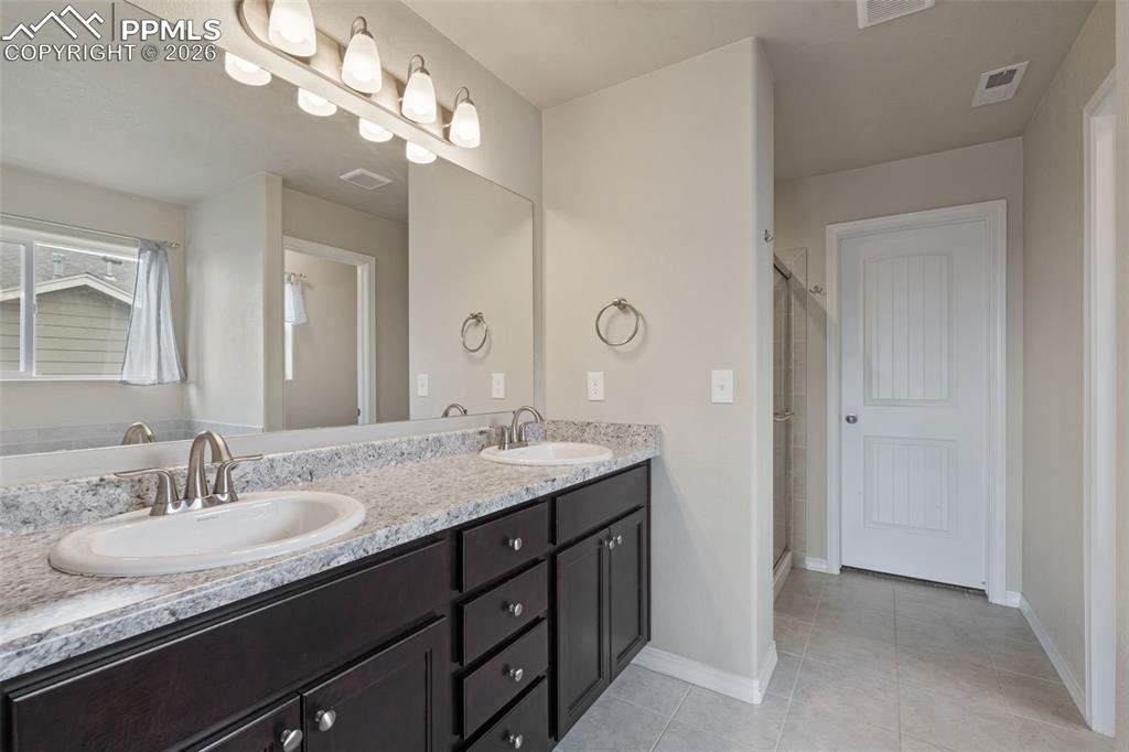 Image 36 of 50: Bathroom with double vanity, a stall shower, and light tile patterned floor