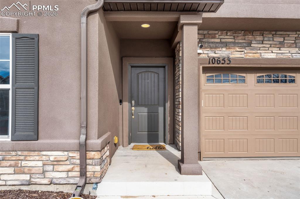 Image 6 of 50: Property entrance with stone siding, a garage, and driveway