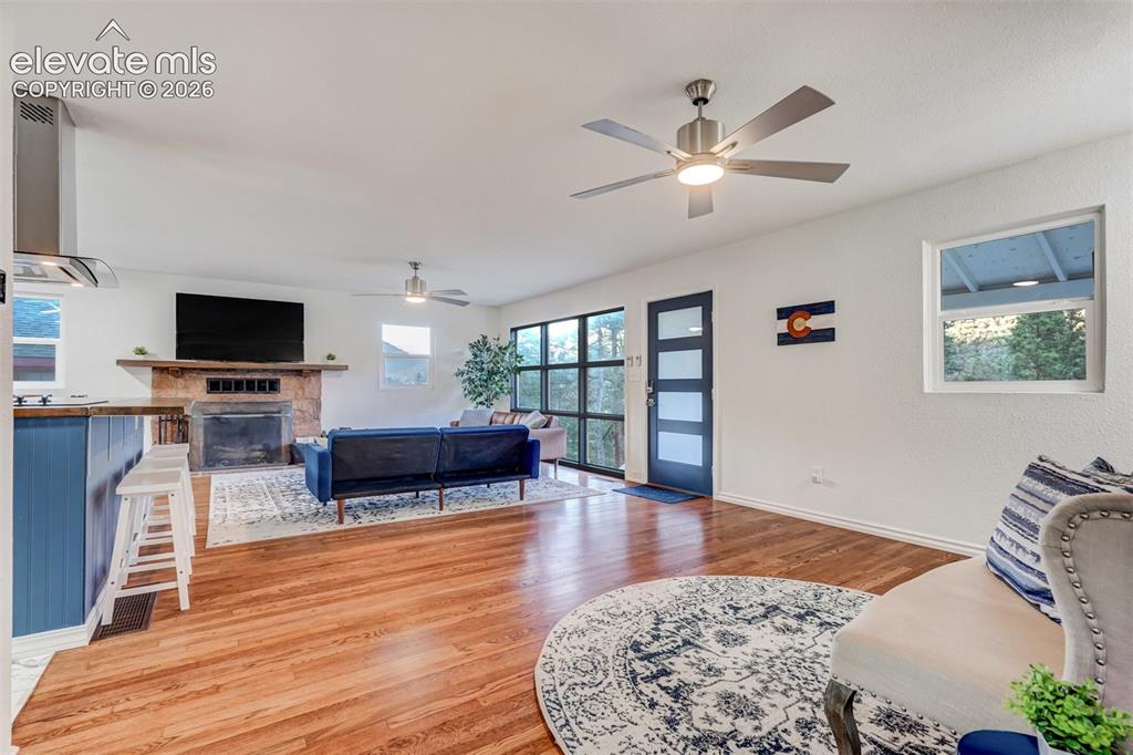 Image 12 of 41: Hardwood flooring, stone-clad fireplace, integrated range hood, modern ceil