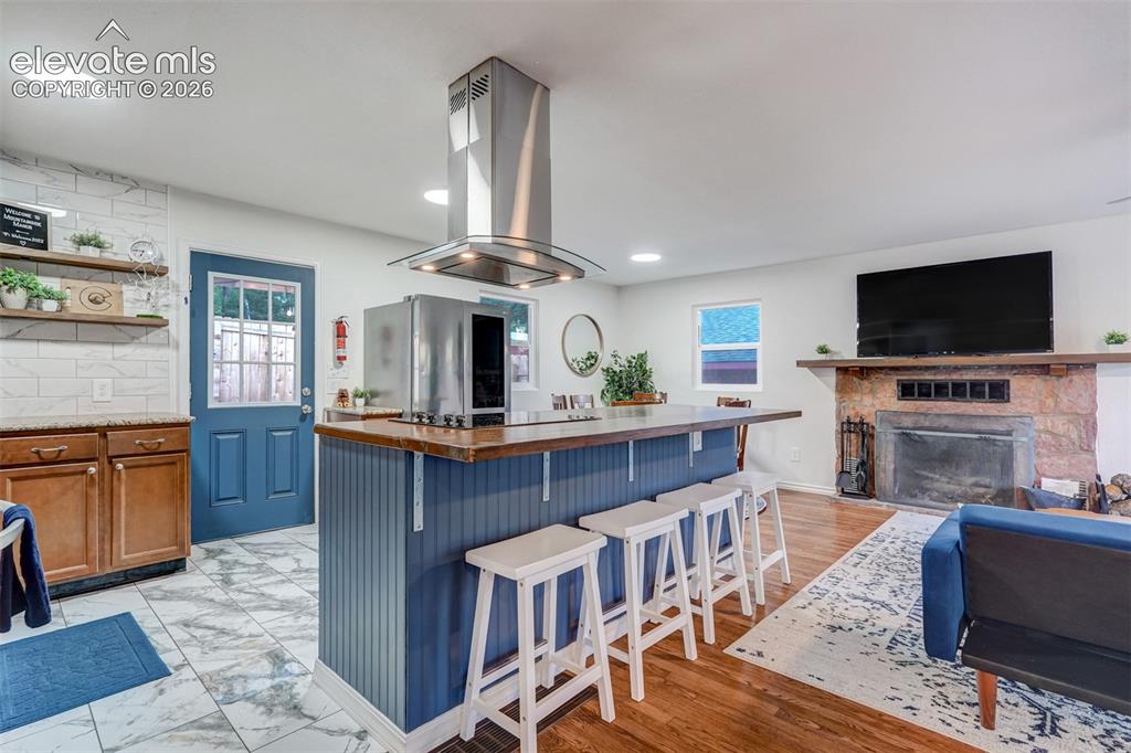 Image 14 of 41: Open-concept living area featuring a kitchen island with seating, a stone f