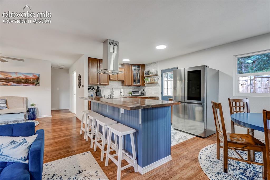 Image 15 of 41: Kitchen island with wood-finish countertop, stainless steel range hood, and