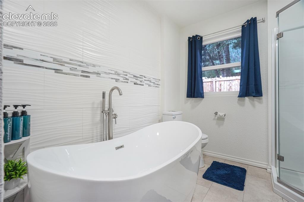 Image 23 of 41: Freestanding soaking tub with floor-mounted faucet, textured tile wall with