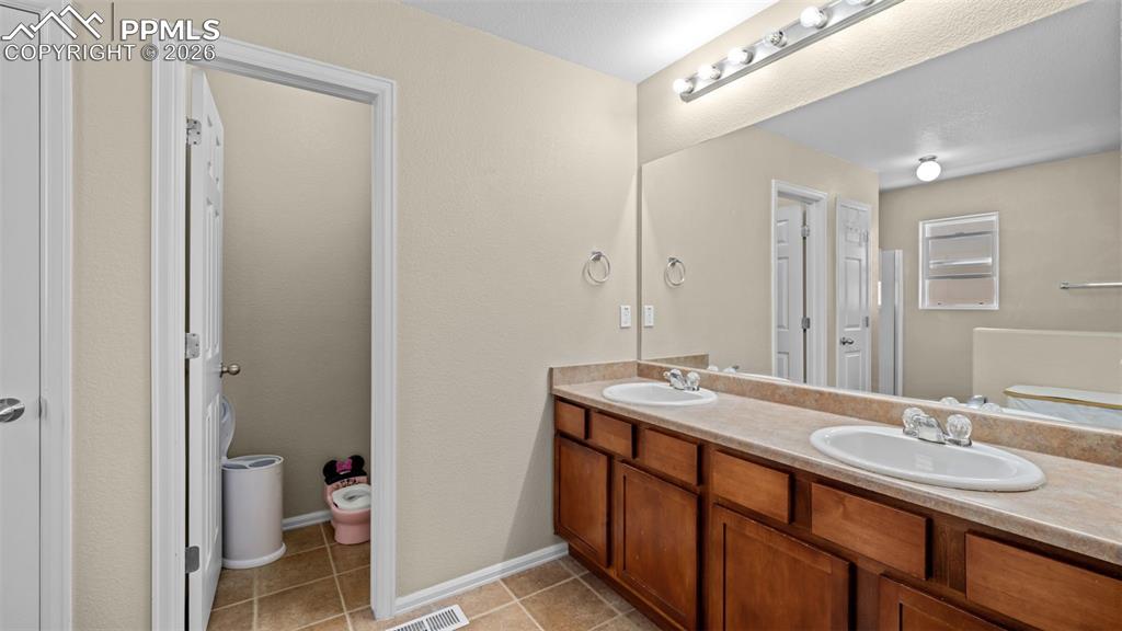 Image 14 of 37: Full bath with double vanity, a bath, light tile patterned floors, and a ce