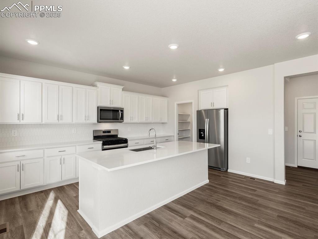 Image 3 of 28: Kitchen featuring stainless steel appliances, white cabinets, dark wood-sty