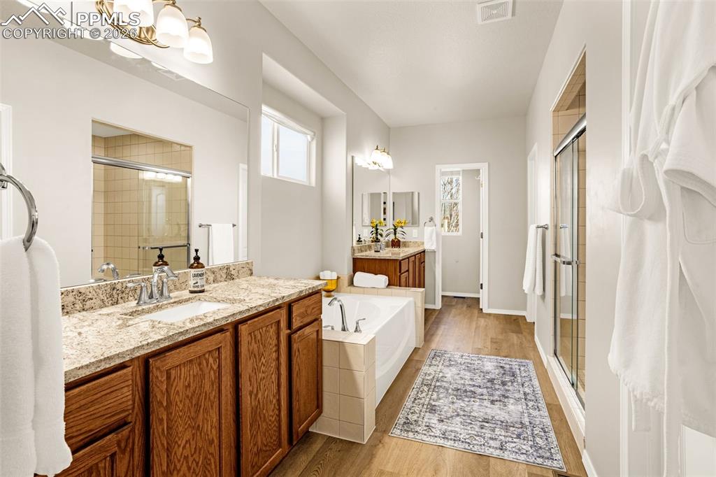 Image 22 of 42: primary bathroom featuring two vanities, a bath, light wood finished floors