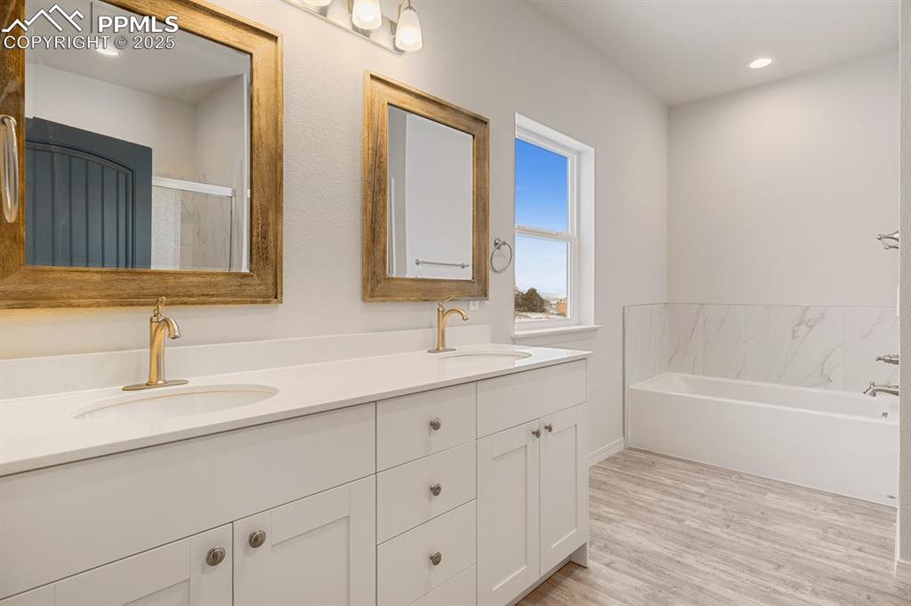 Image 20 of 22: Full bath featuring double vanity, a bath, wood finished floors, recessed l
