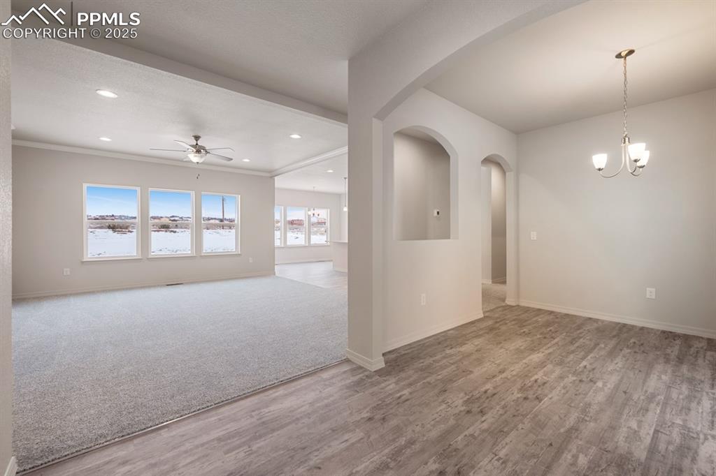 Image 3 of 22: Empty room with ceiling fan, wood finished floors, a chandelier, recessed l