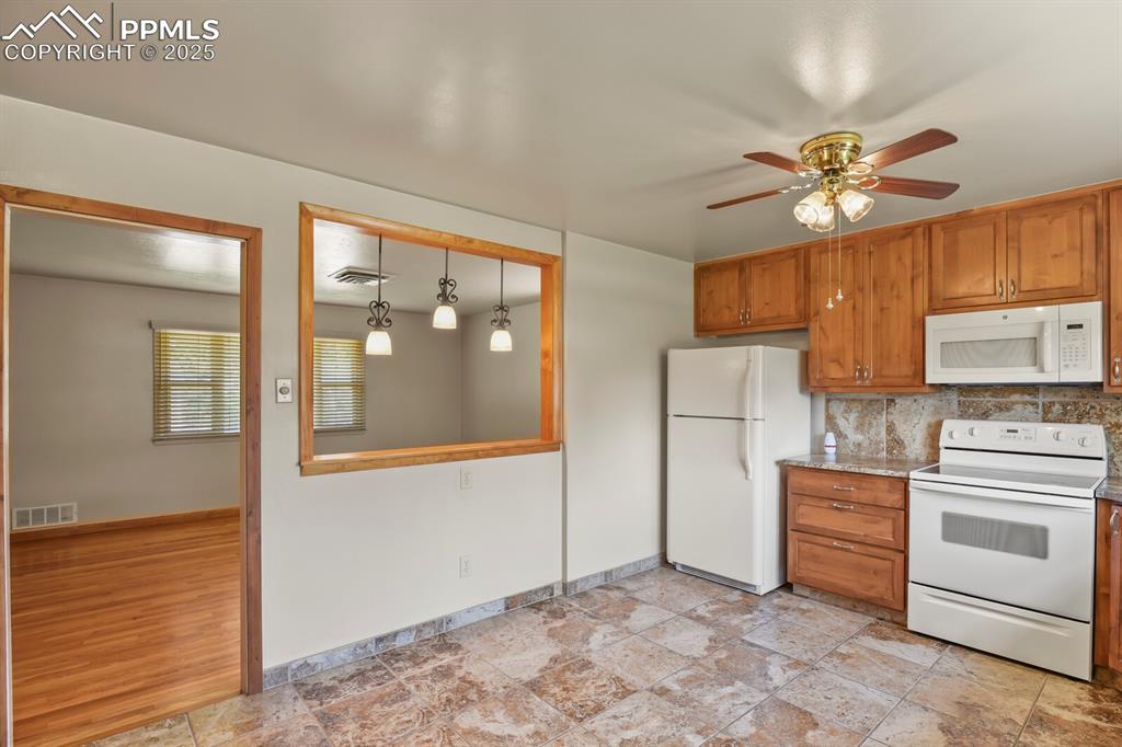 Image 10 of 24: Kitchen with white appliances, brown cabinetry, a ceiling fan, and tasteful