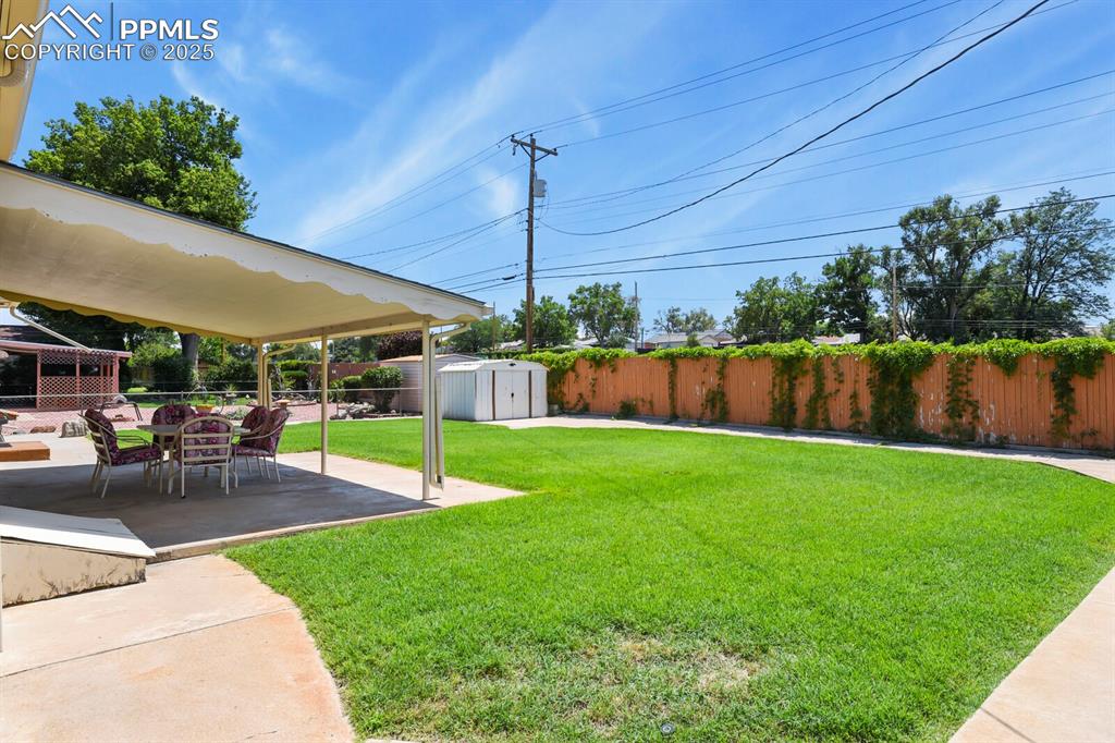 Image 19 of 24: Fenced backyard with a storage shed and covered concrete patio