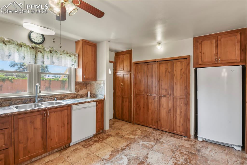 Image 9 of 24: Kitchen with white appliances, solid wood cabinets, ceiling fan, and backsp