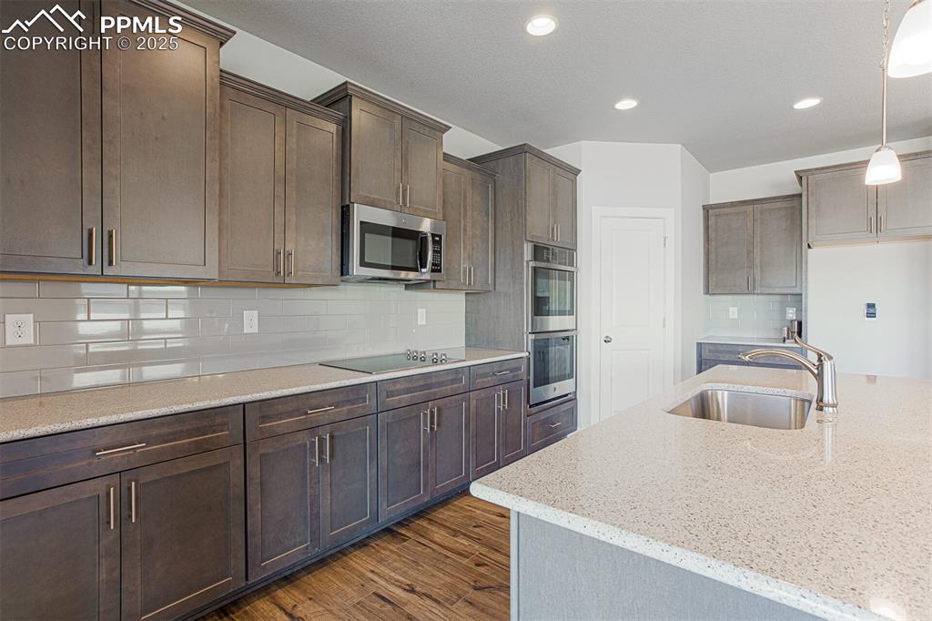 Image 3 of 10: Kitchen featuring tasteful backsplash, light stone counters, dark brown cab