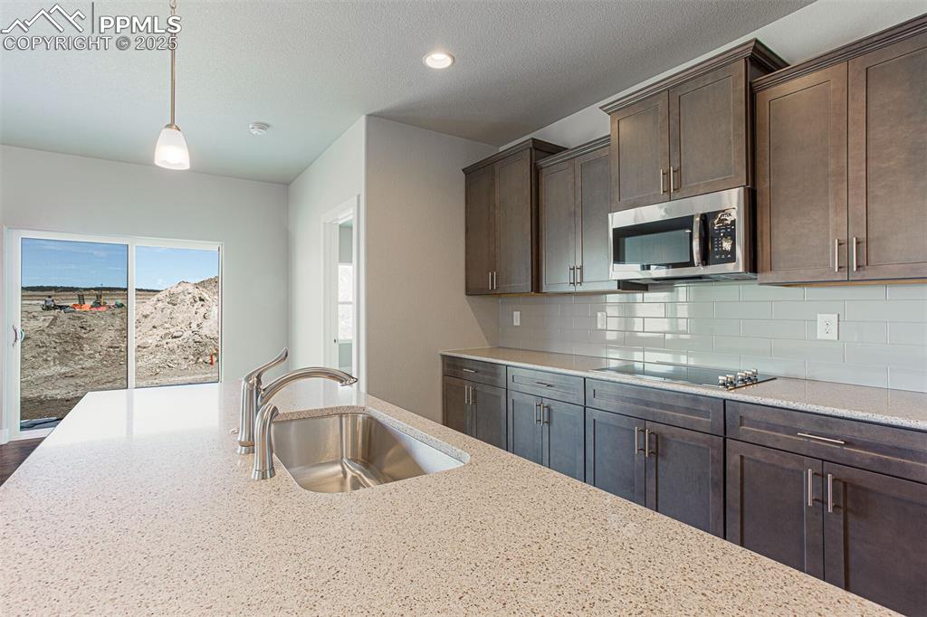 Image 4 of 10: Kitchen with dark brown cabinets, light stone counters, stainless steel mic