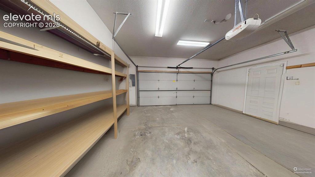 Image 28 of 31: Spacious garage featuring a concrete floor, built-in wood shelving, a panel