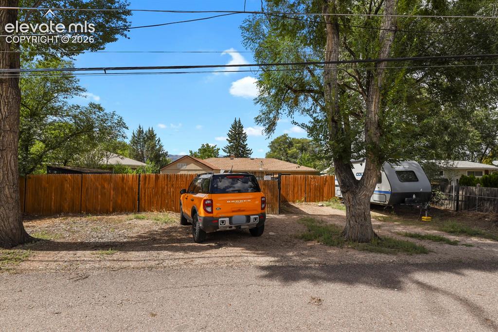 Image 26 of 28: Gravel driveway with mature trees and wood fence