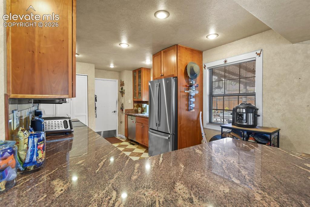 Image 6 of 28: Kitchen featuring a stone-look countertop, wood cabinetry, recessed lightin
