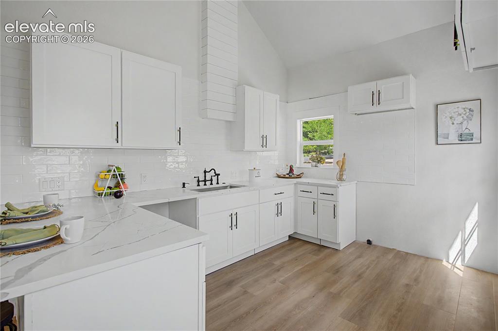 Image 5 of 19: Kitchen featuring wood-finish flooring, white cabinetry, a white subway til