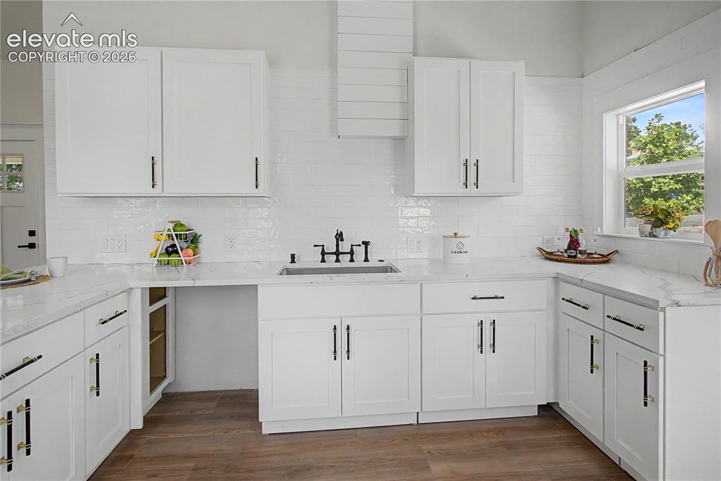 Image 6 of 19: White shaker cabinetry, wood-finish flooring, subway tile backsplash, white