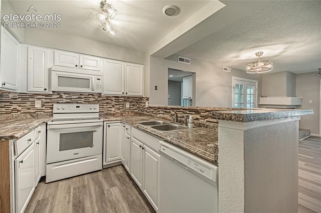 Image 6 of 37: Kitchen featuring wood-finish flooring, white cabinetry, a mosaic tile back