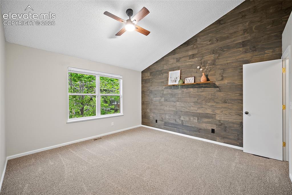 Image 10 of 37: Vaulted ceiling room featuring a wood-panel accent wall with built-in shelv