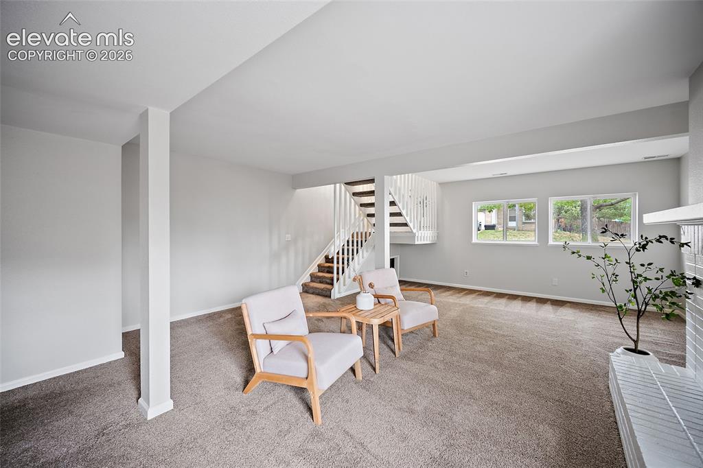 Image 22 of 37: Spacious living area featuring neutral carpeting, a white baluster staircas