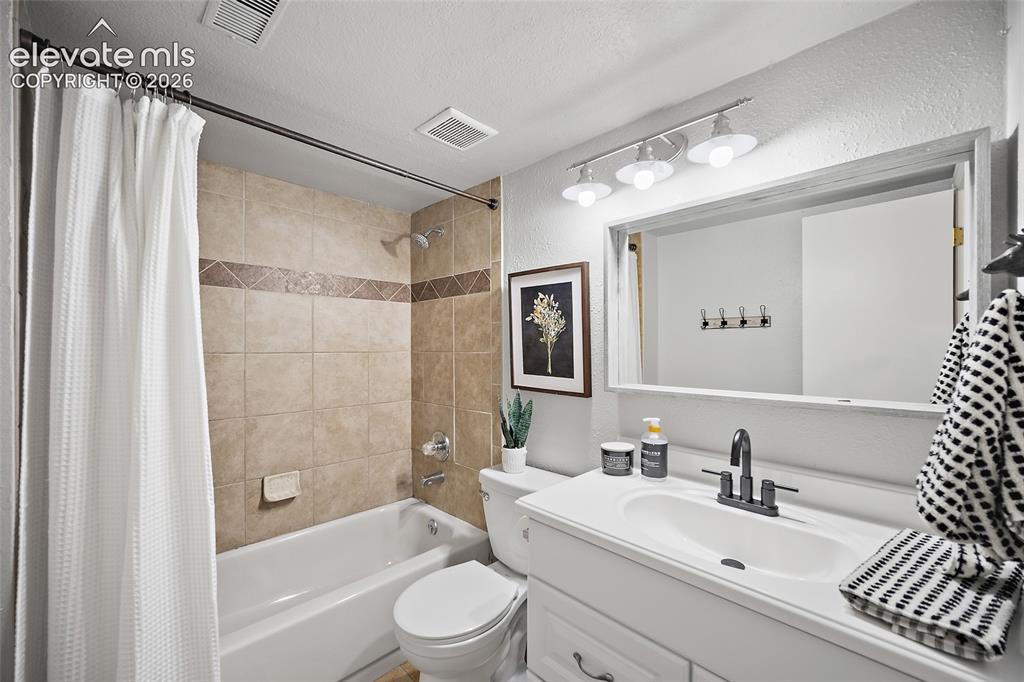 Image 24 of 37: Bathroom featuring a white vanity with an integrated sink, a dark-finish fa