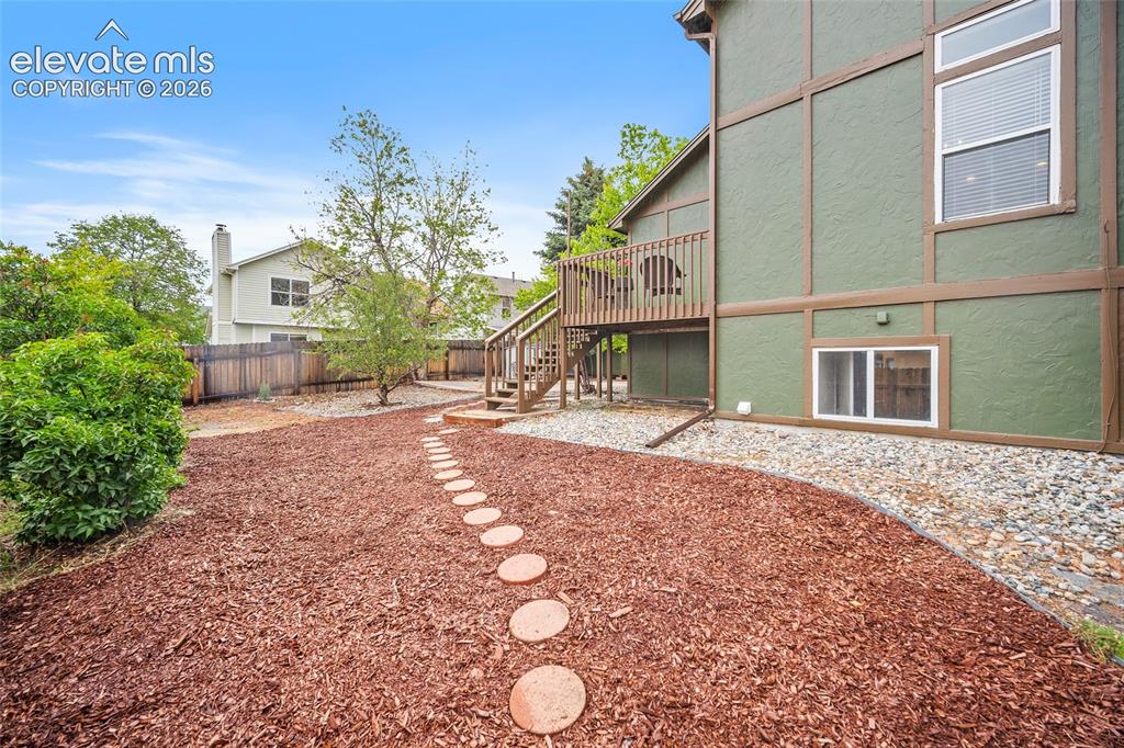 Image 34 of 37: Rear exterior featuring a wood deck with stairs, a stone path, and a ground