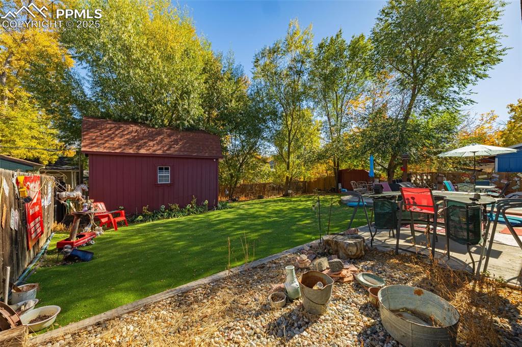 Image 18 of 25: Fenced backyard with a patio and an outbuilding