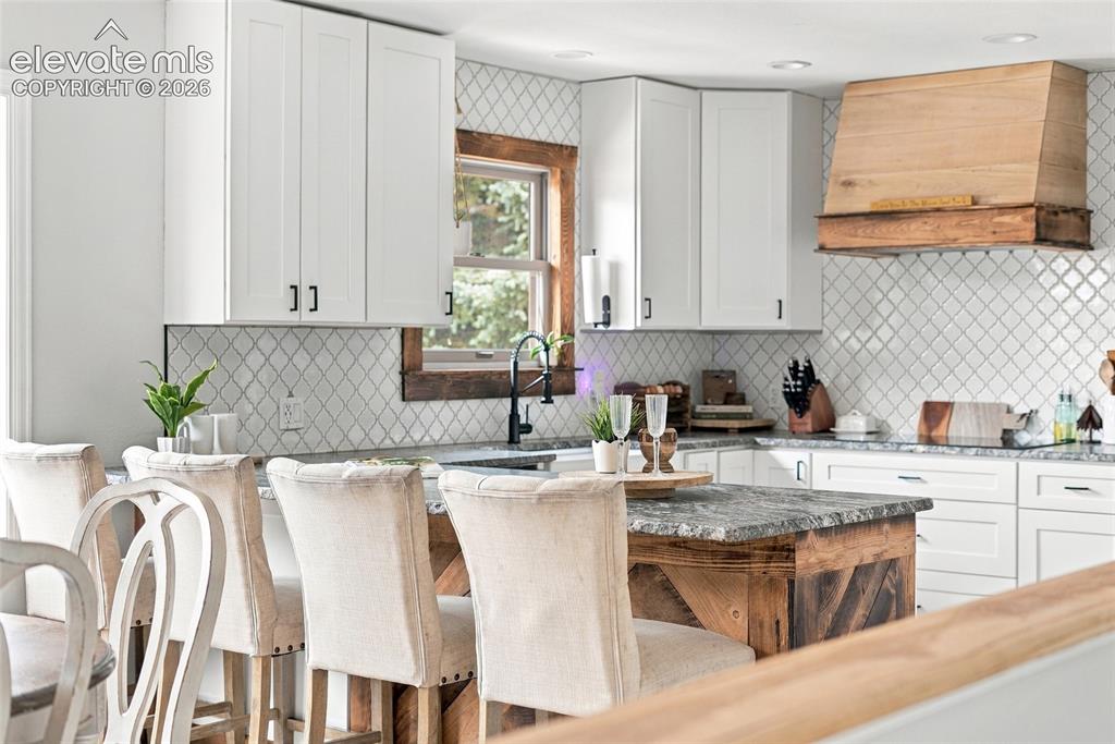 Image 15 of 49: White shaker-style cabinetry with matte black hardware, textured tile backs