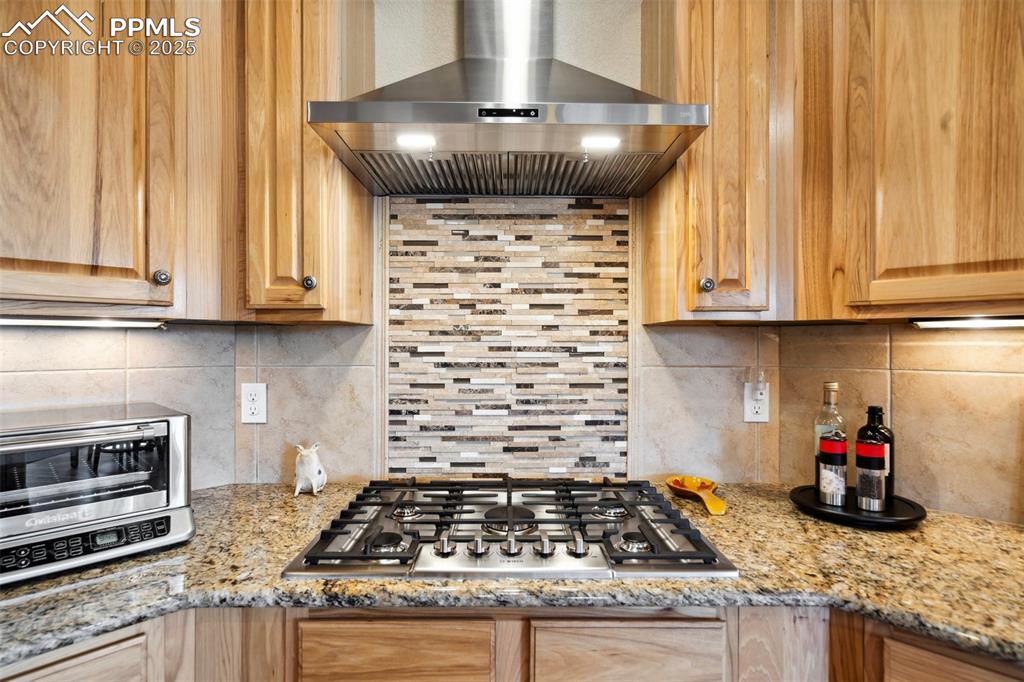 Image 14 of 46: Kitchen featuring tasteful backsplash, hood, stainless steel gas cooktop,