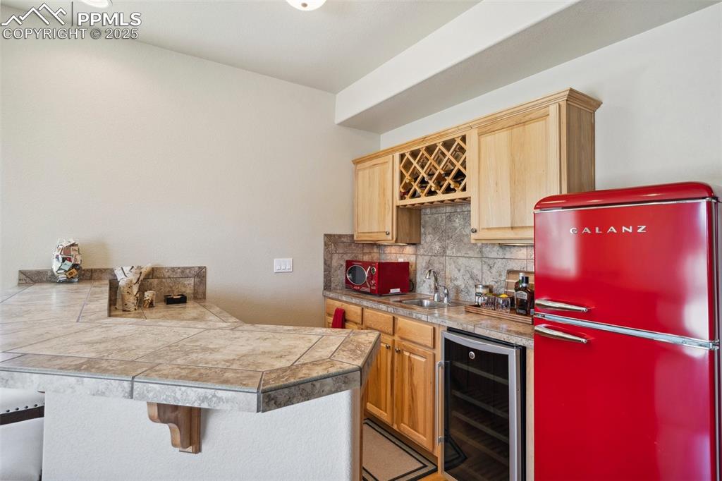 Image 27 of 46: Bar featuring tasteful backsplash, wet bar, freestanding refrigerator, wine