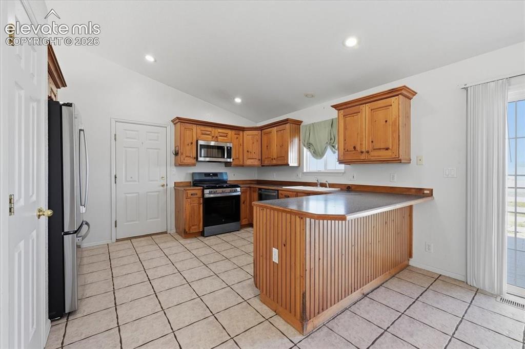 Image 13 of 46: Kitchen featuring wood cabinetry, stainless steel microwave, and tile floor