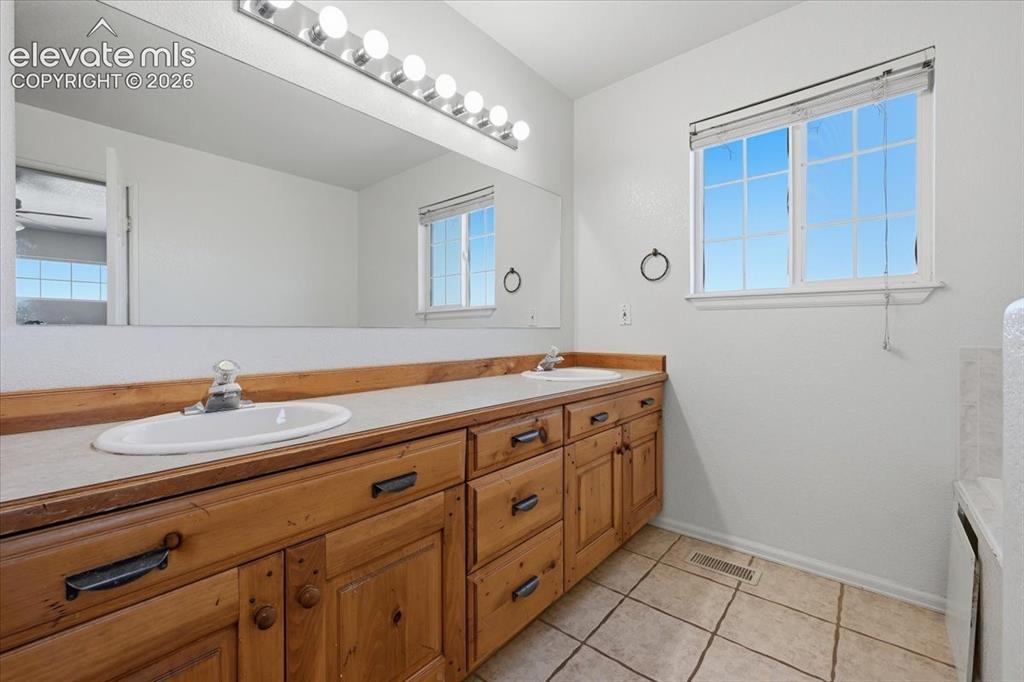 Image 16 of 46: Dual basin vanity with wood-finish cabinetry, a large mirror, and overhead