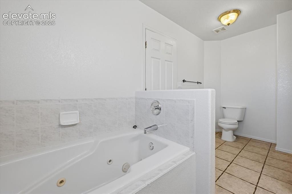 Image 18 of 46: Soaking tub with chrome fixtures, tiled surround, white paneled door, ceram