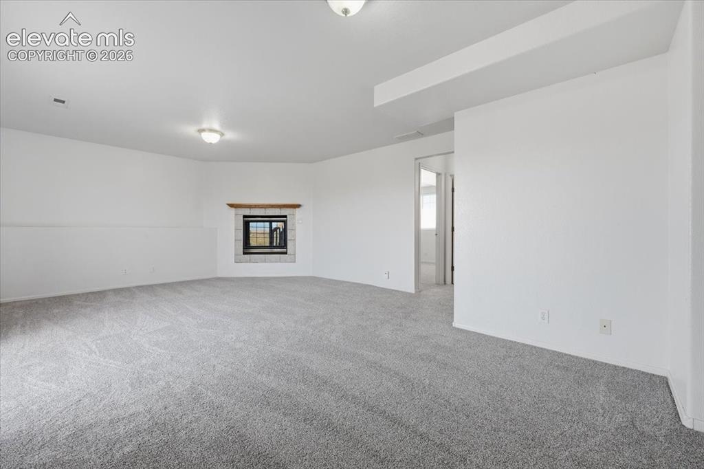 Image 24 of 46: Spacious room with light gray carpeting, a built-in fireplace featuring a s